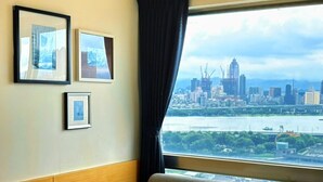 A hotel room with a bed, a sofa, a window with a city view, and three framed pictures on the wall. - We Meet Taipei Hotel (New Taipei City)