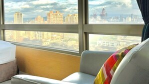 A hotel room with a large window offering a view of a cityscape with multiple buildings and a bridge. - We Meet Taipei Hotel (New Taipei City)