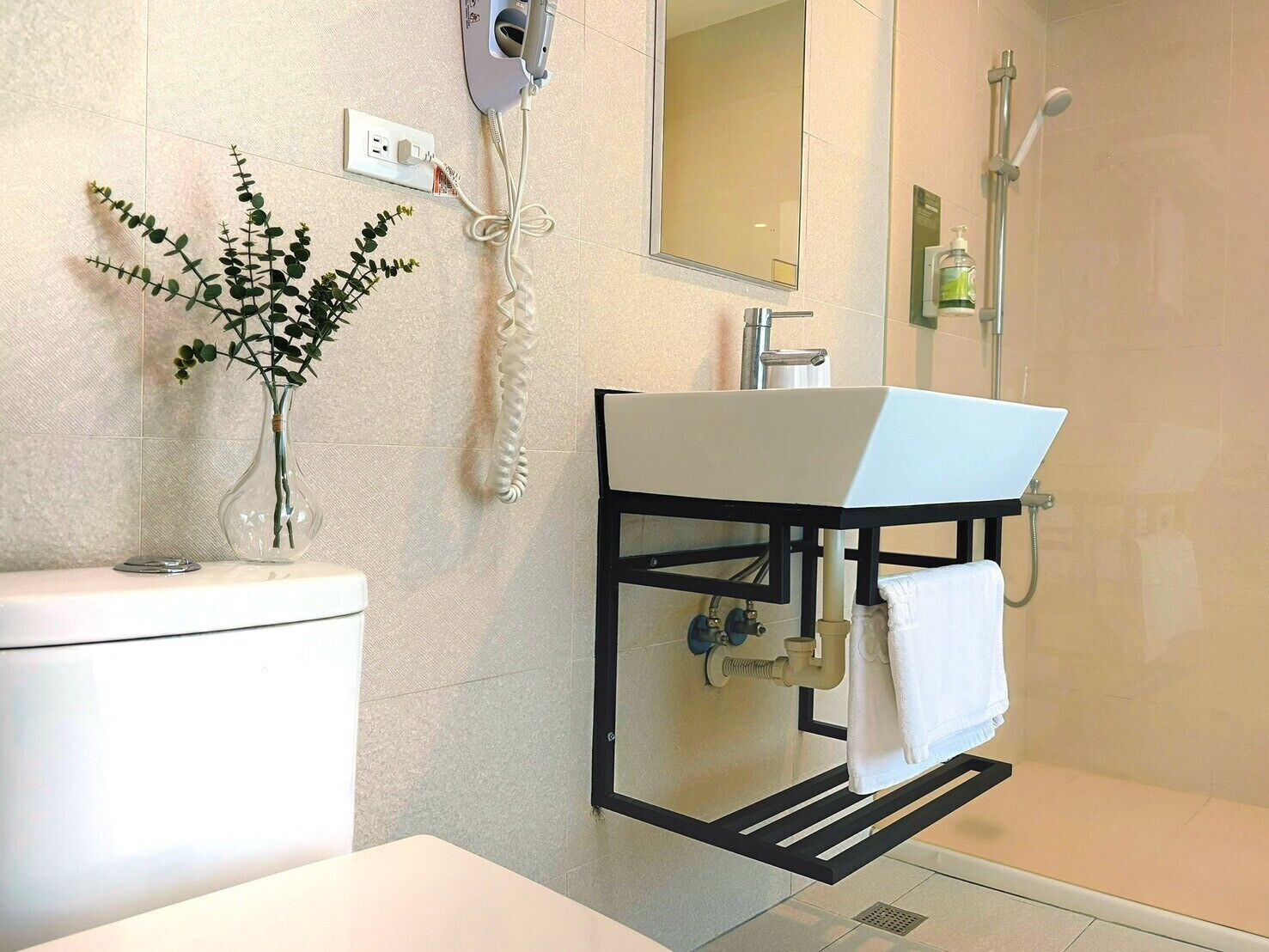 A modern bathroom with a white sink, a mirror, a shower, and a plant on the wall.