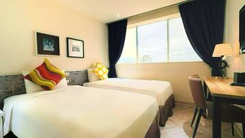 A hotel room with two beds, a desk, a chair, a lamp, and a window with curtains.