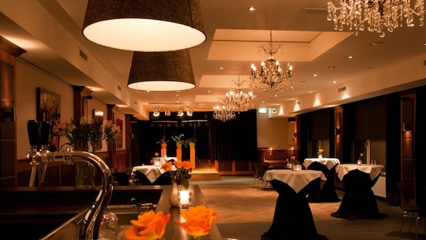 A well-lit dining area with tables set for service, a bar area with a sink, and a chandelier. - Hotel St. Lambert (Helmond)