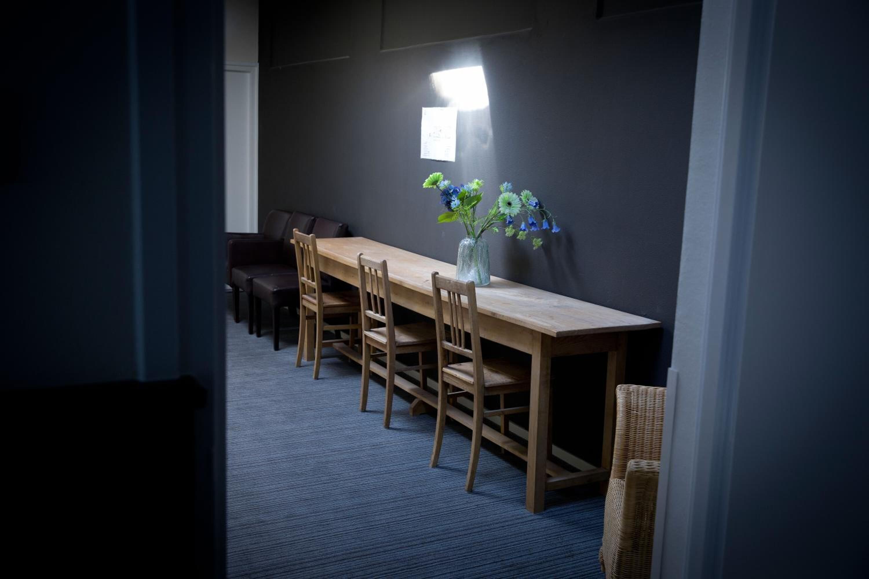 Un comedor con una larga mesa de madera, varias sillas y un florero con flores en la pared.