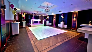 A spacious room with a large dance floor, a chandelier, and a stage area. - Hotel St. Lambert (Helmond)