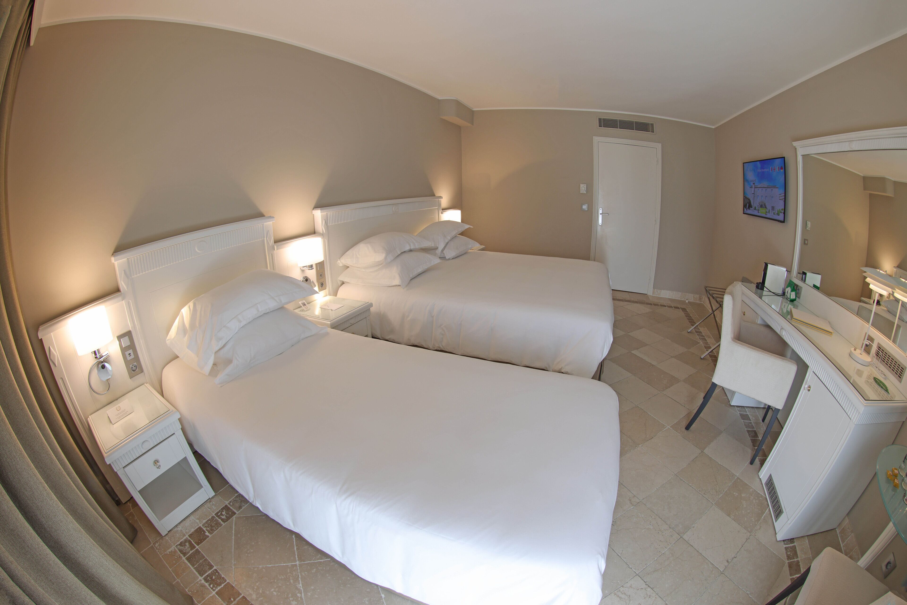 A hotel room with two beds, a desk with a chair, a mirror, and a door.