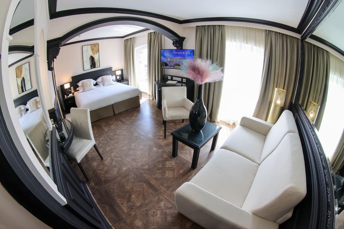 Quarto de hotel com uma cama, um sofá, uma TV e um vaso com penas decorativas.