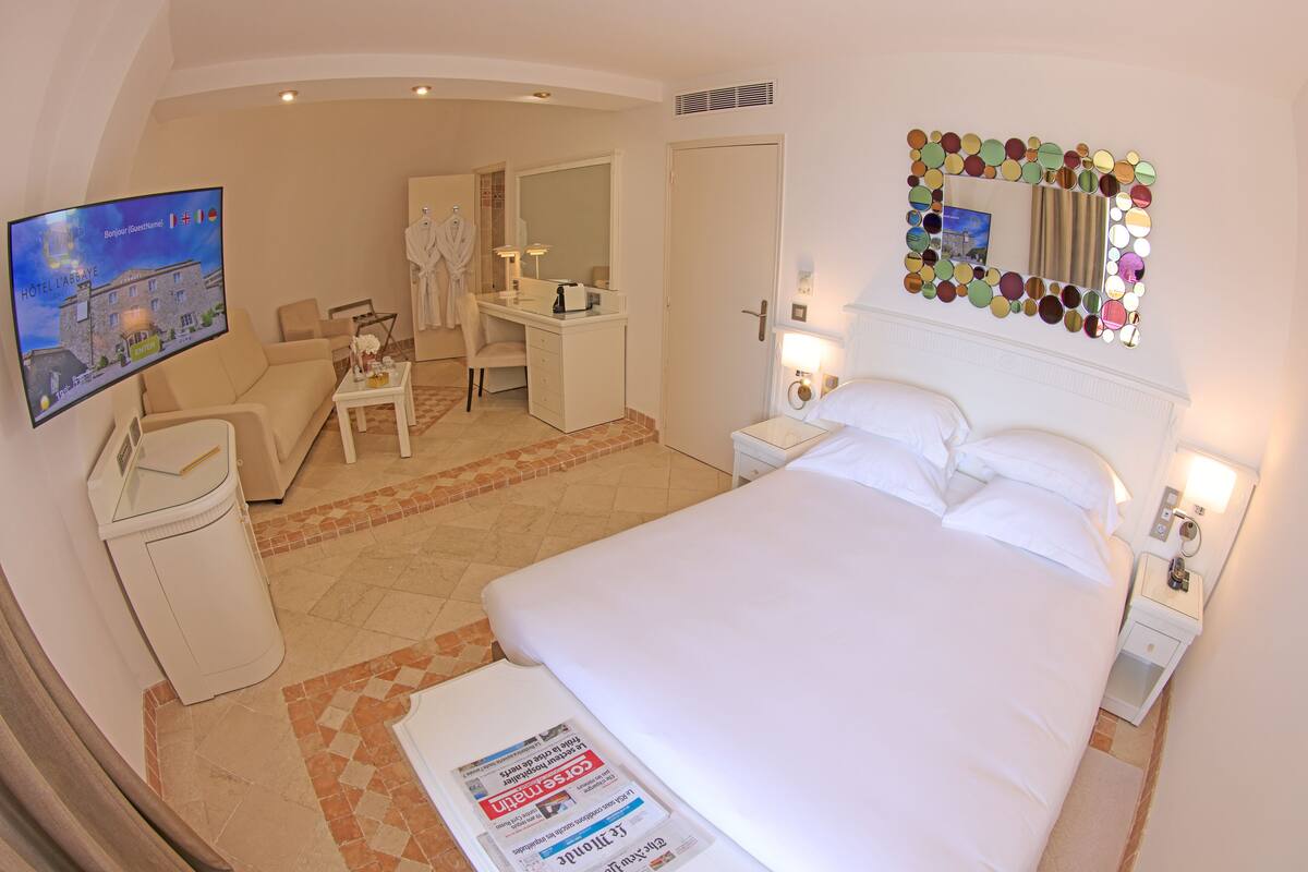 Quarto de hotel com cama, escrivaninha, cadeira, televisão, banheiro e espelho com moldura decorativa.