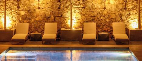 A pool area with lounge chairs and a stone wall backdrop.