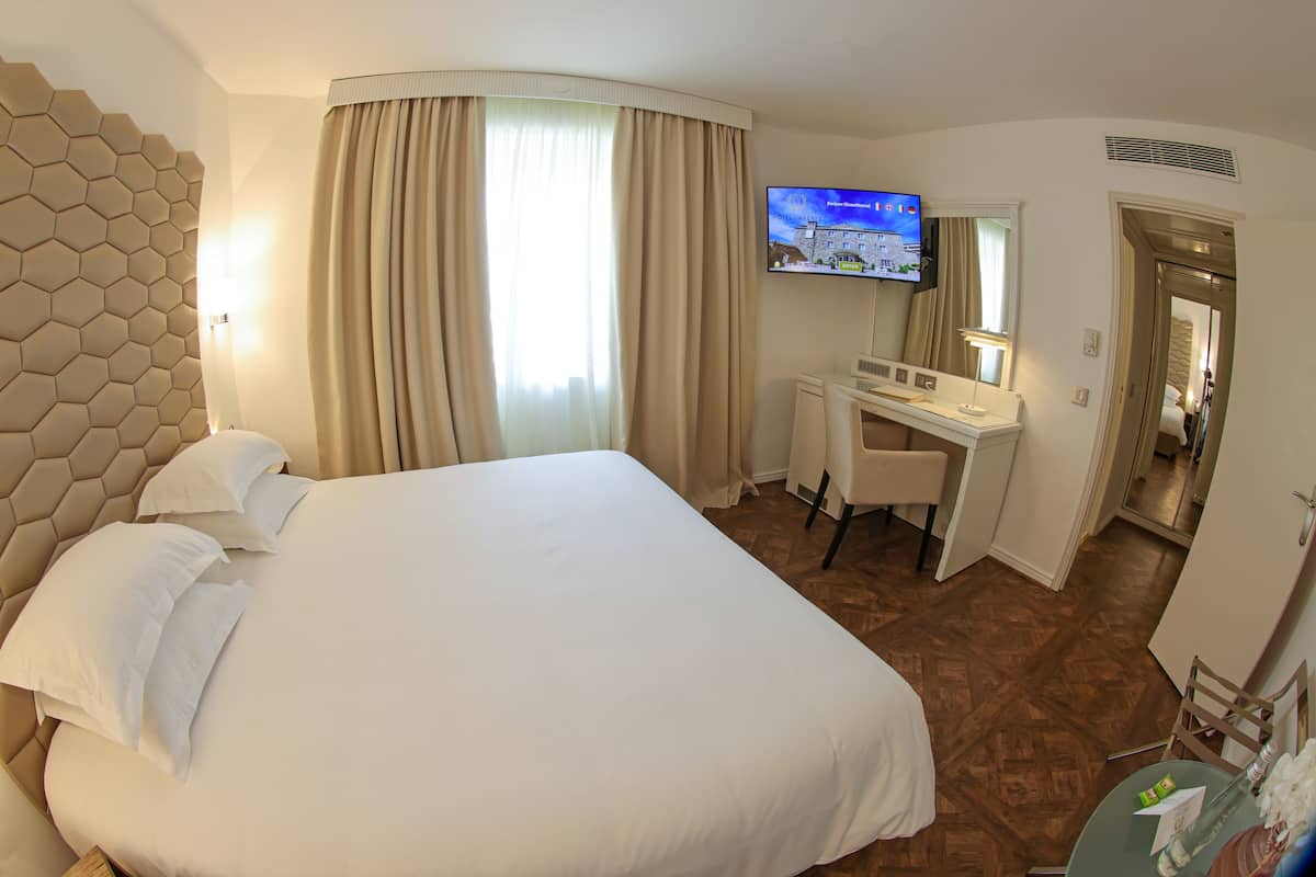 Quarto de hotel com uma cama grande, uma escrivaninha, uma televisão e um banheiro visível através de uma porta aberta.