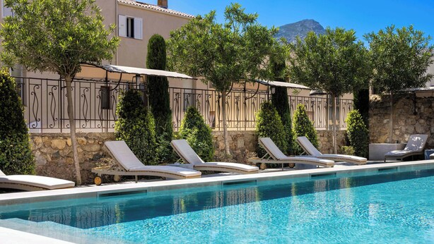 A pool with lounge chairs and a stone wall.