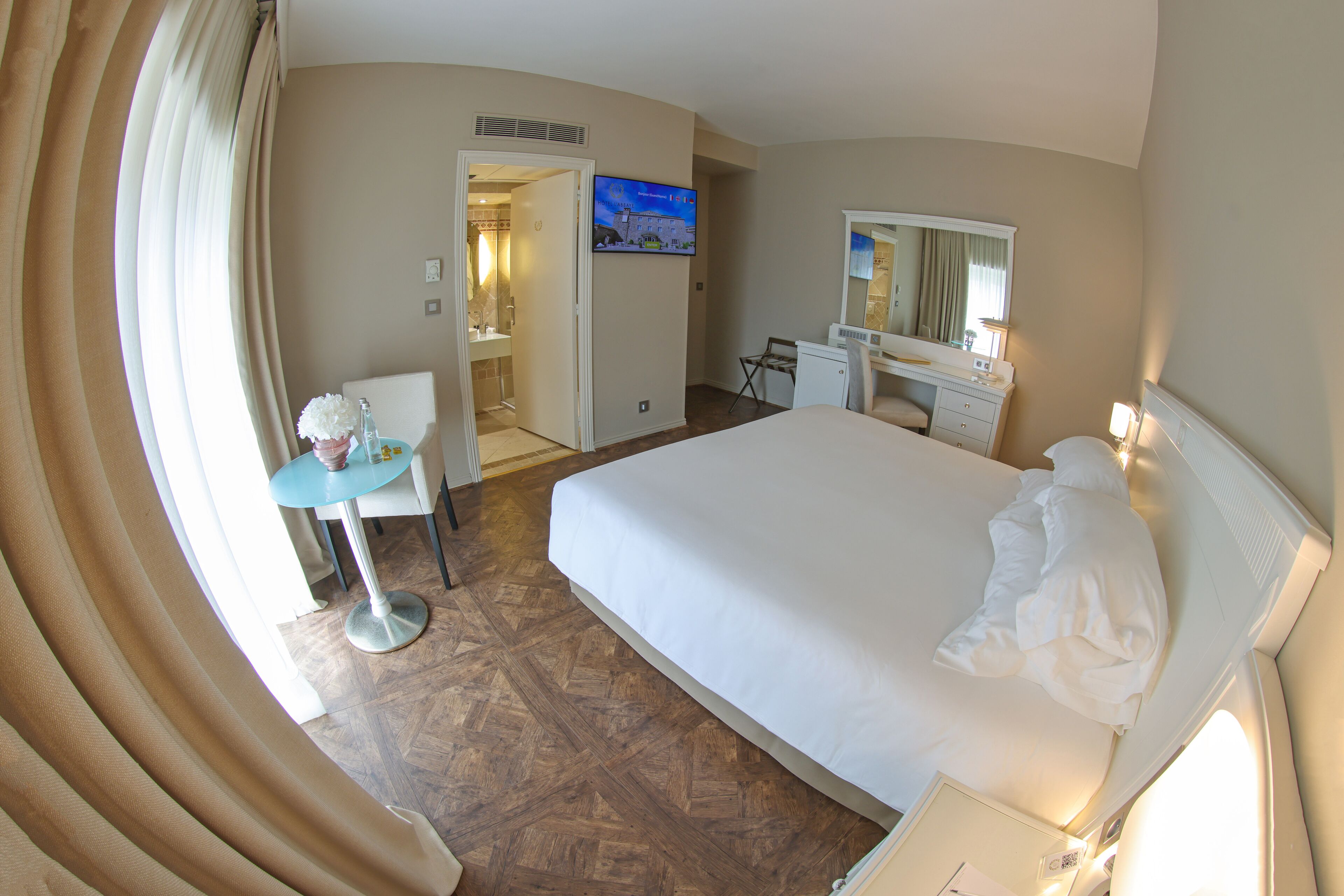 A hotel room with a large bed, a desk with a chair, a television, and a bathroom visible through an open door.