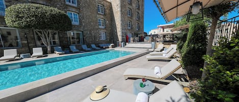 A poolside area with lounge chairs, a swimming pool, and a stone building in the background.