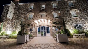 A stone building with a large arched entrance, potted plants, and outdoor seating.