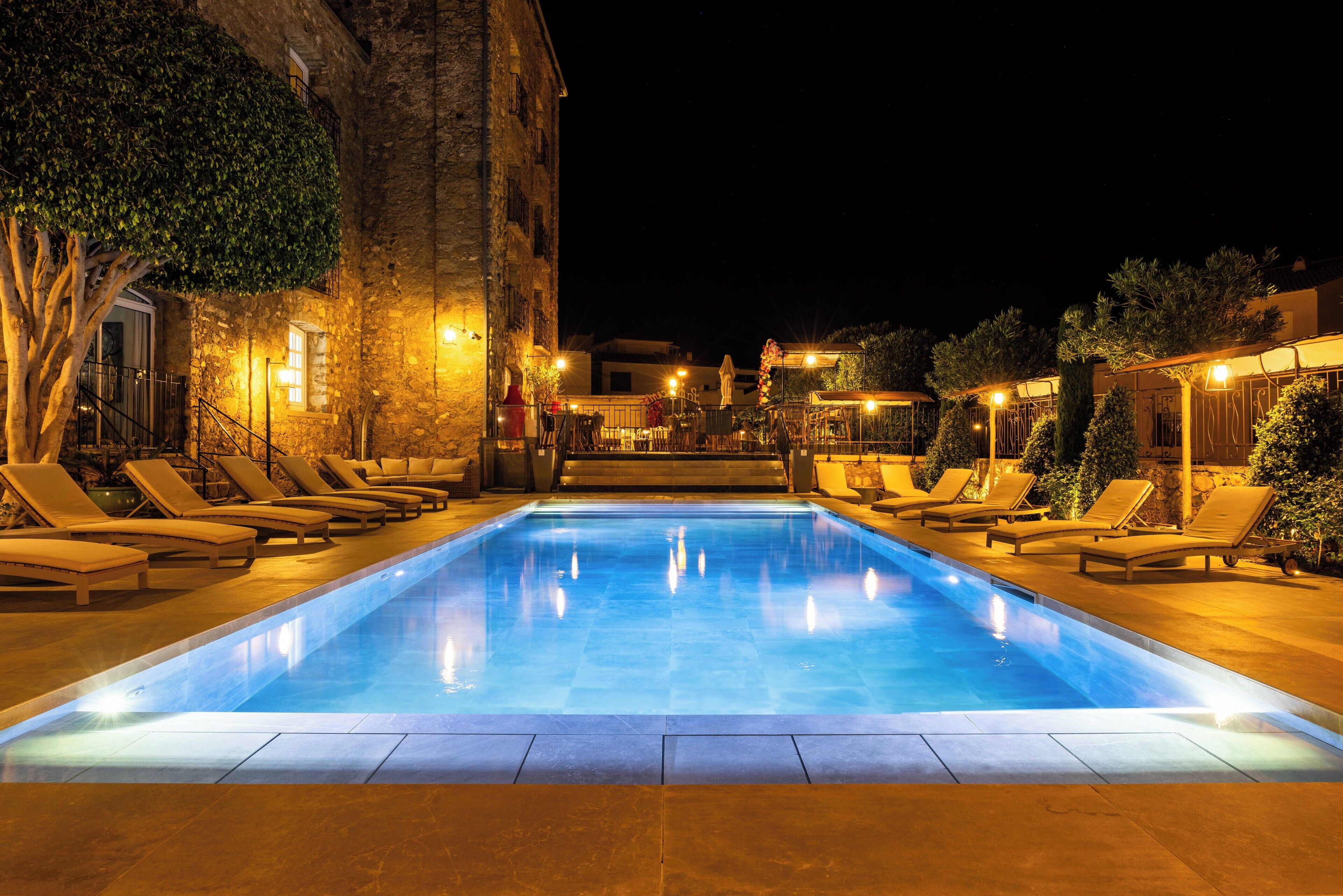 A swimming pool with lounge chairs and a stone building at night.