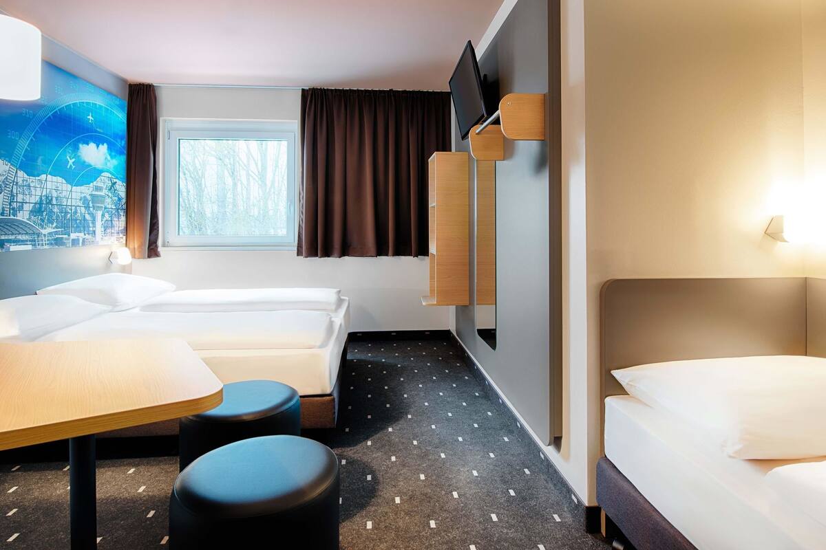 A hotel room with two beds, a desk, and a large window.