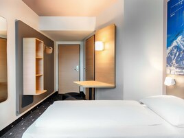 A hotel room with a bed, a mirror, a shelf, and a poster on the wall.