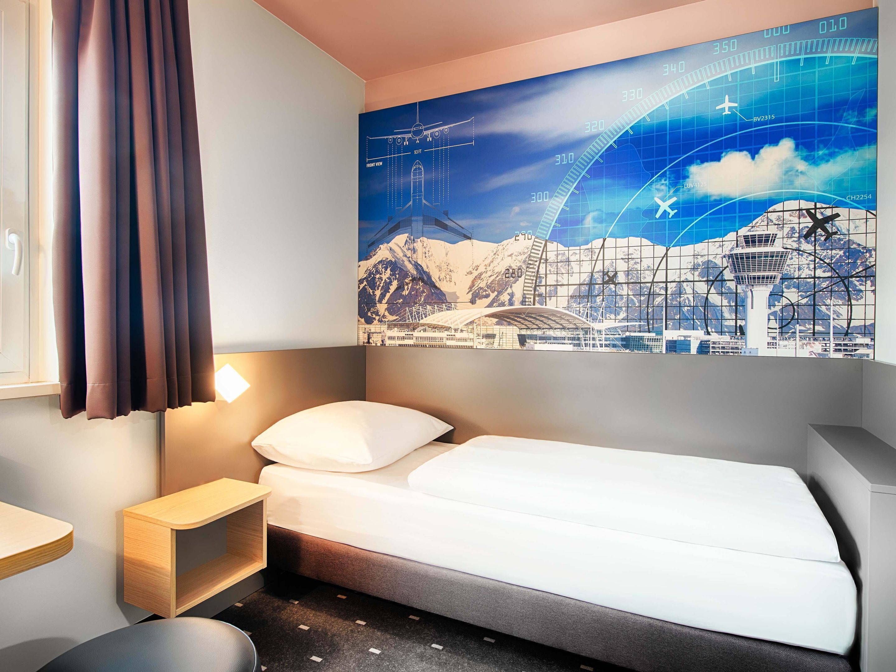 Une chambre d’hôtel avec un lit, une table de chevet, une lampe et une grande fenêtre avec des rideaux.