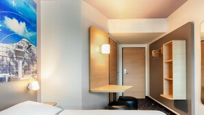 A hotel room with a bed, a desk, a chair, a mirror, and a wall-mounted shelf. - B&B Hotel München-Airport (Hallbergmoos)