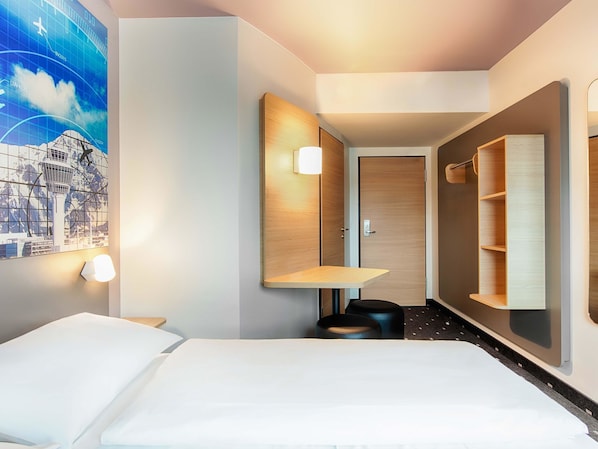 Een hotelkamer met een bed, een bureau, een stoel, een spiegel en een wandplank.