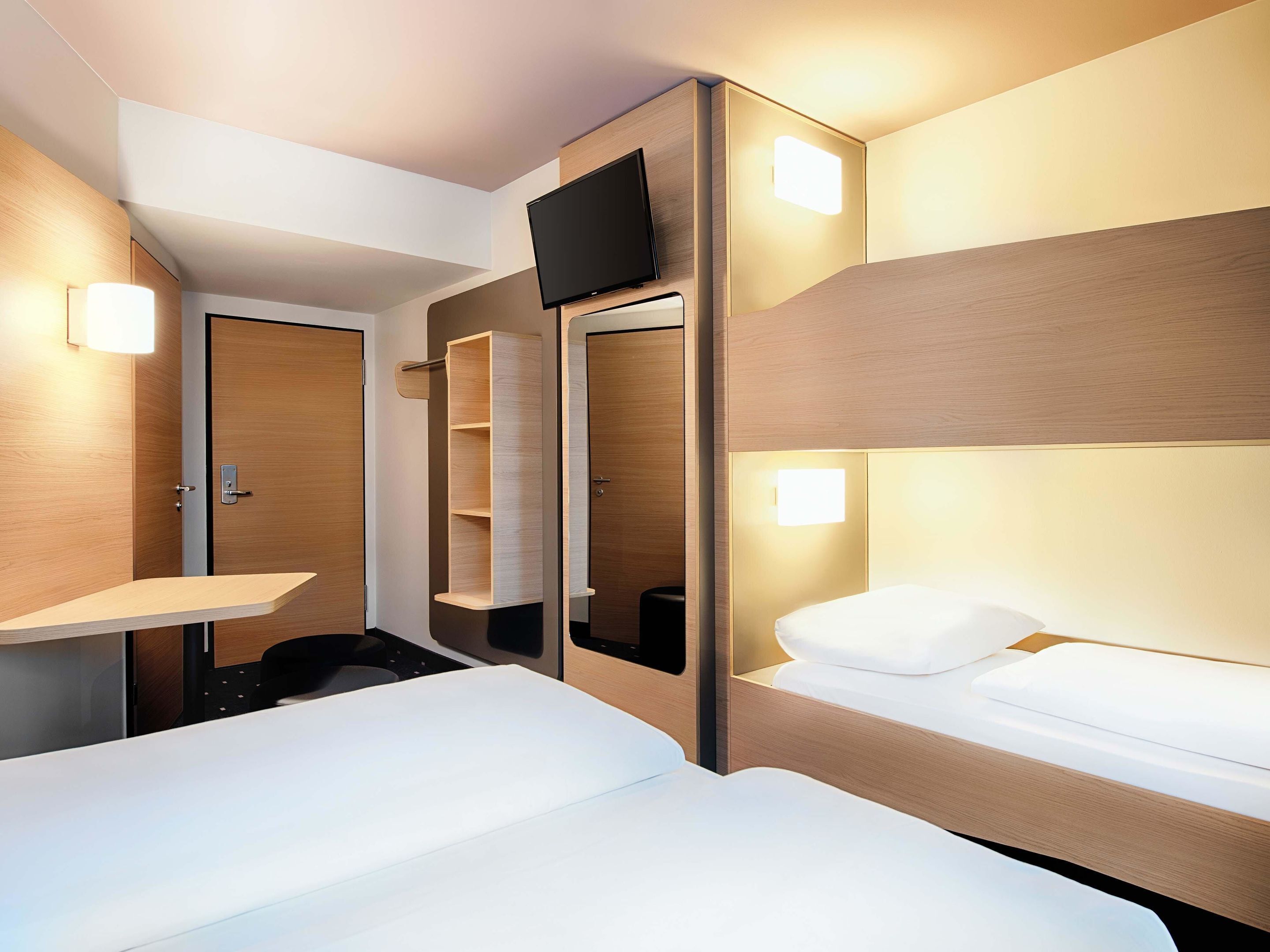Ein Hotelzimmer mit Etagenbetten, einem Flachbildfernseher, einem Nachttisch und einer Schrankwand.