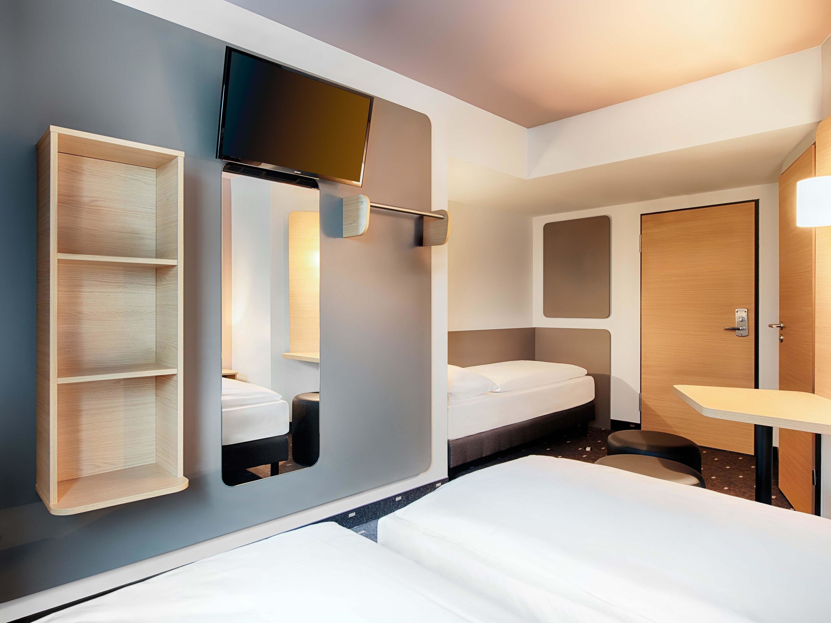 Una camera d'albergo moderna con un letto, una TV a muro, una piccola scrivania e un armadio.
