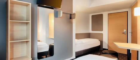 A modern hotel room with a bed, a TV mounted on the wall, a small desk, and a wardrobe.