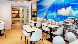A modern restaurant with a large digital wall displaying flight paths and a mountainous landscape. - B&B Hotel München-Airport (Hallbergmoos)
