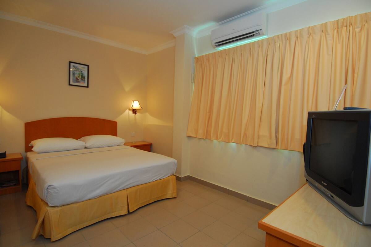 A hotel room with a bed, a nightstand, a lamp, an air conditioner, and a television.