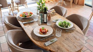 Une table de salle à manger en bois, avec deux assiettes de nourriture, une bouteille d’huile d’olive et un vase rempli de fleurs.