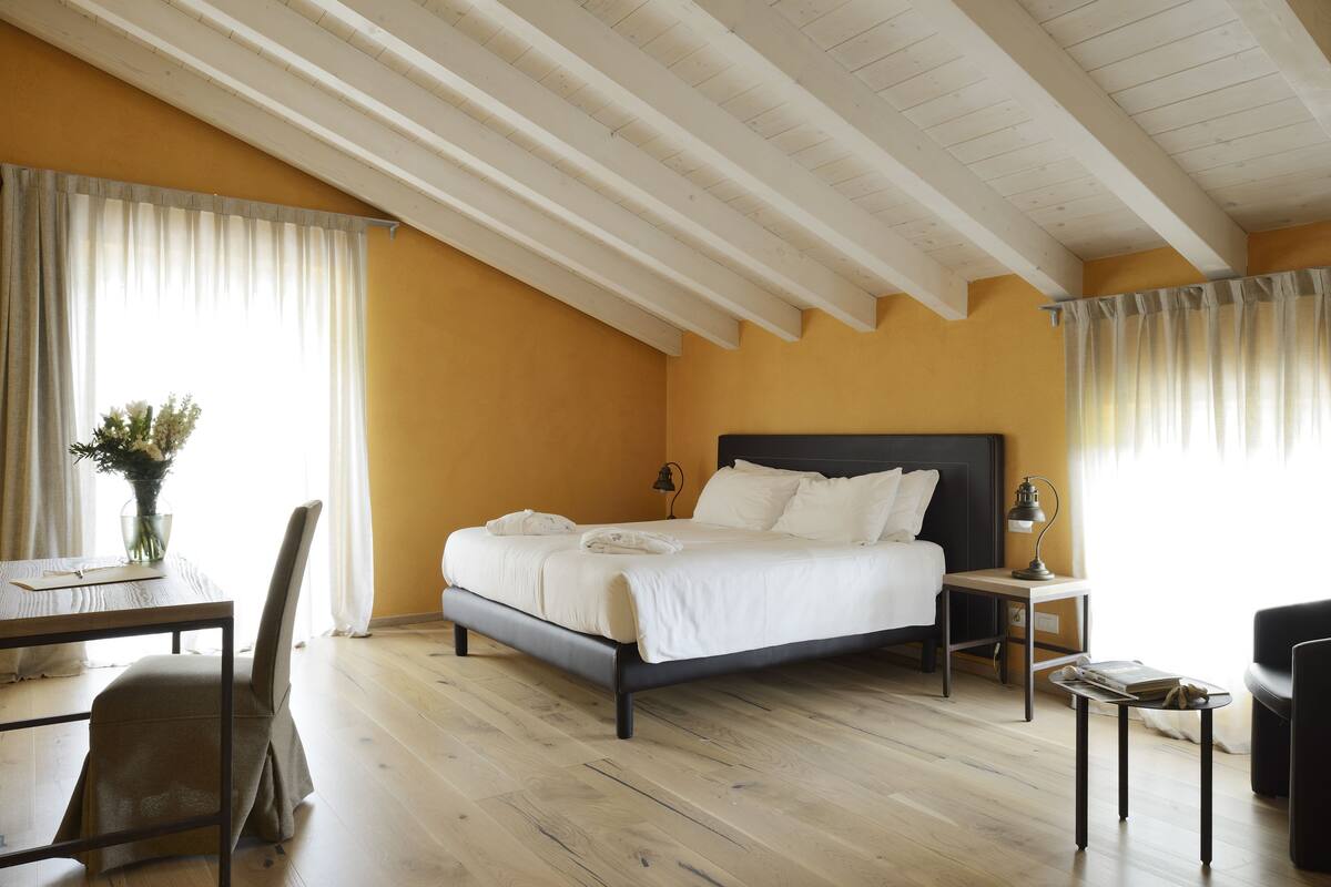 A bedroom with a bed, bedside tables, a chair, a small table, and a lamp.