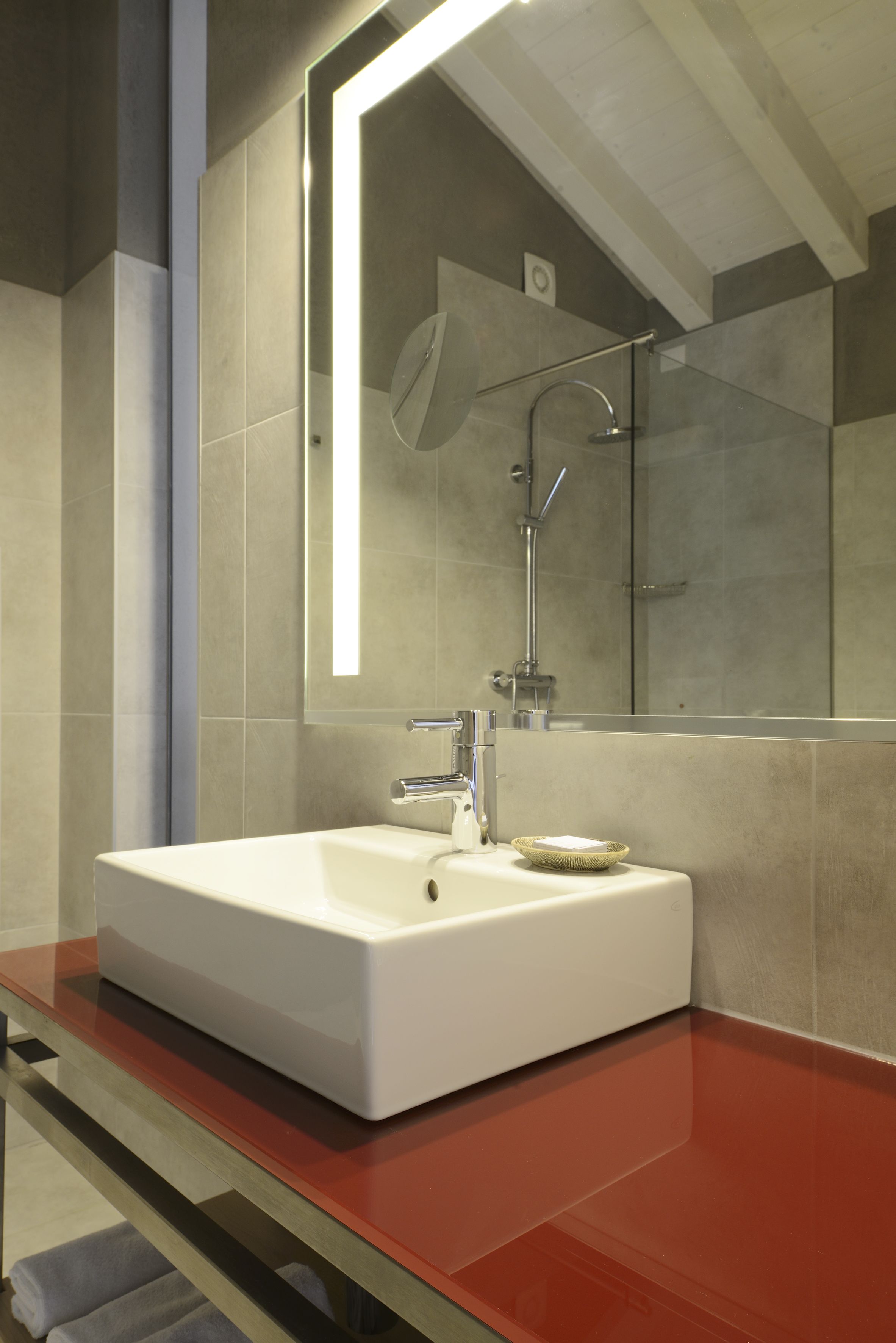 A modern bathroom with a white sink, a glass shower enclosure, and a large mirror.