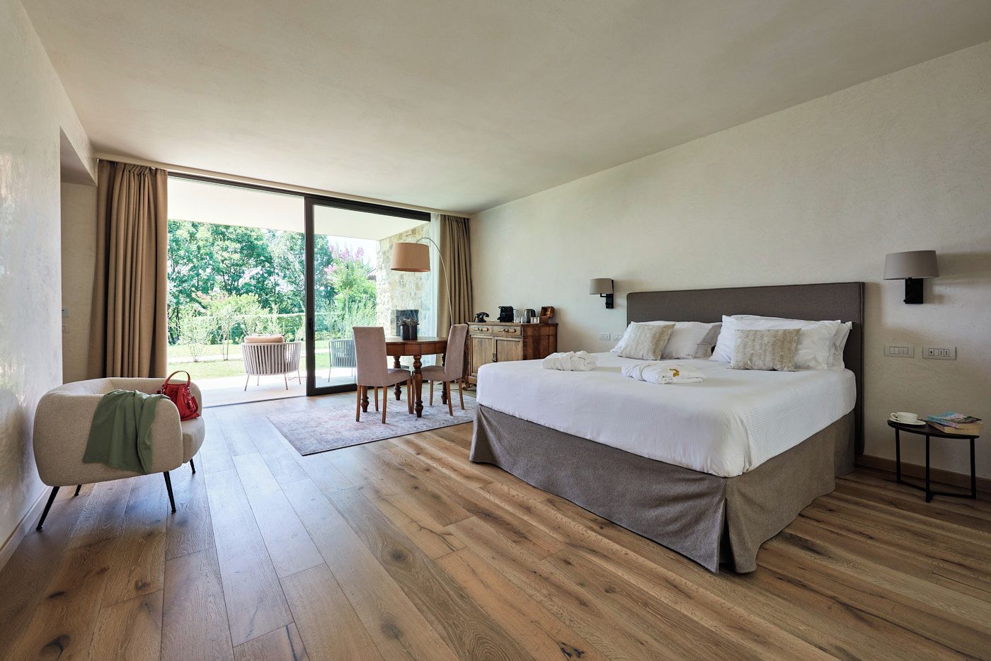 A hotel room with a large bed, a dining table, and a view of the outdoors.