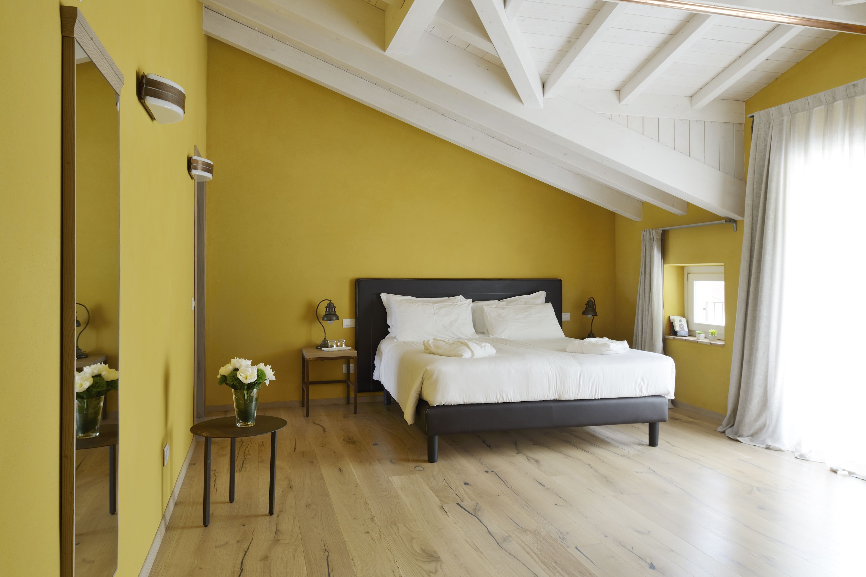 A bedroom with a bed, bedside tables, a mirror, and a window with curtains.