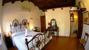Un dormitorio con cama, escritorio, silla, espejo y un baño visible a través de una puerta abierta.