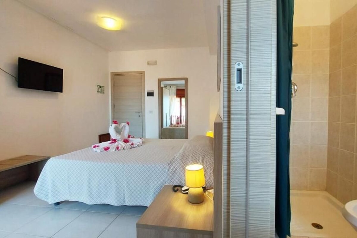 A hotel room with a bed, bedside table with a lamp, a TV mounted on the wall, and a bathroom with a bathtub and sink.
