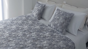 Una cama con colcha y almohadas estampadas, un cuadro de una estrella de mar en la pared y un interruptor de luz.