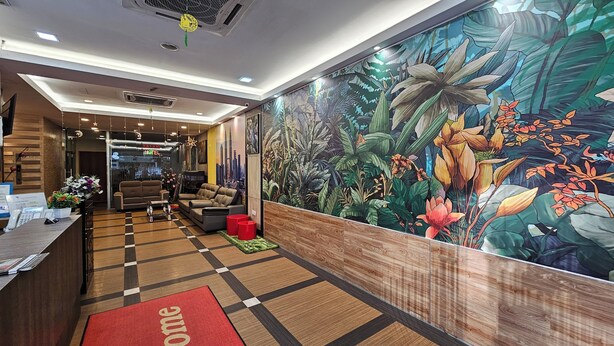 A hotel reception area with a check-in desk, sofas, a large floral mural, and a view of the city skyline. - Safari Hotel (Ampang)