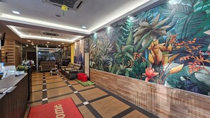 A hotel reception area with a check-in desk, sofas, a large floral mural, and a view of the city skyline. - Safari Hotel (Ampang)
