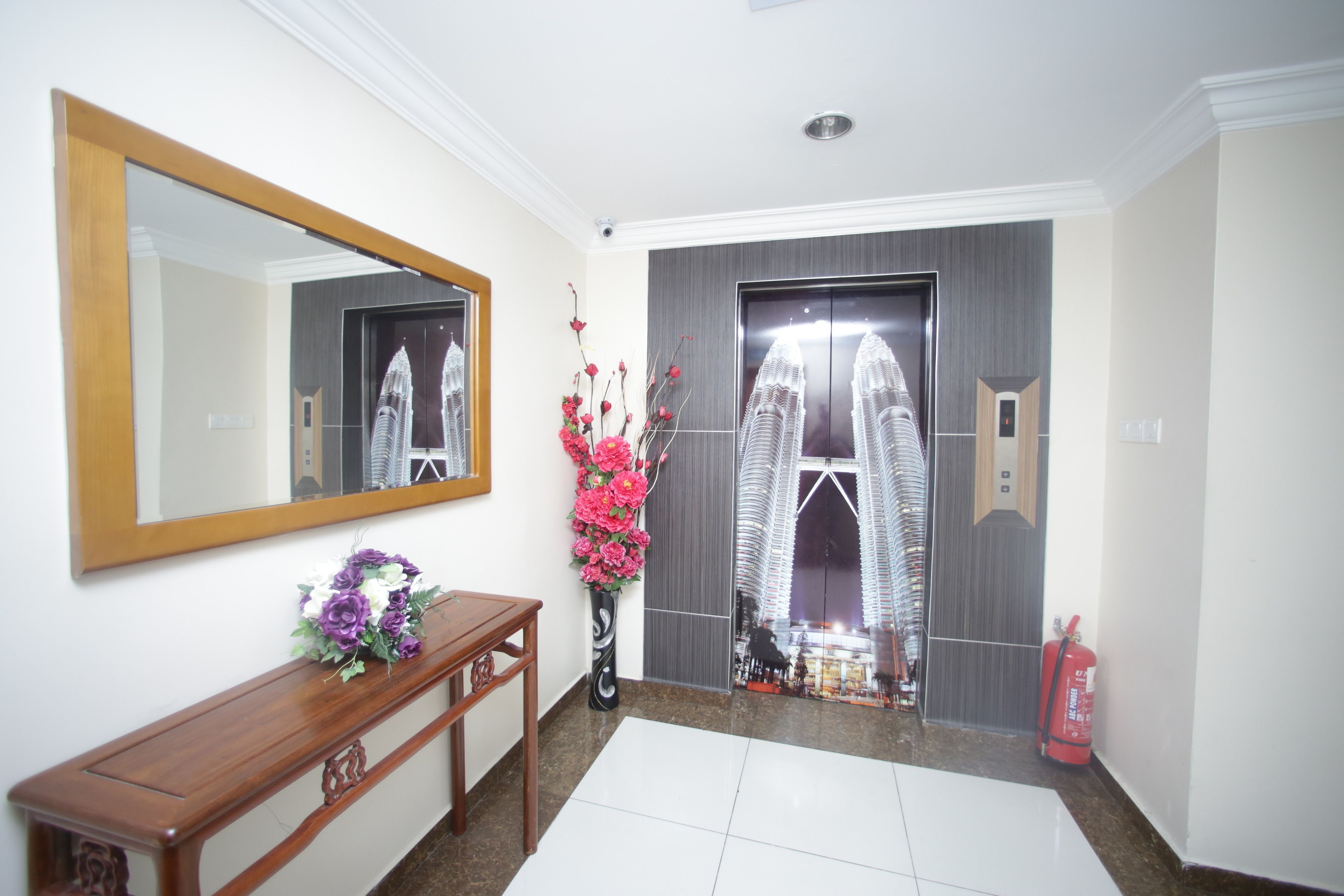 A hallway with a wooden console table, a mirror, a vase with flowers, and a door with a reflection of a building.