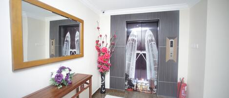 A hallway with a wooden console table, a mirror, a vase with flowers, and a door with a reflection of a building.