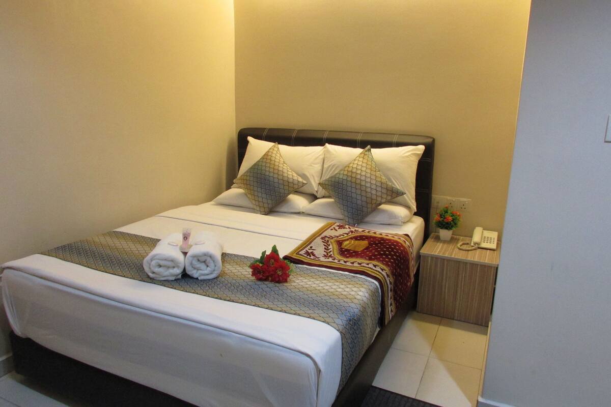 A hotel room with a neatly made bed, a bedside table with a phone, and a small potted plant.