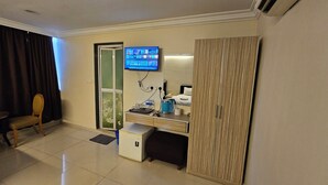 A hotel room with a desk, a television mounted on the wall, a small cabinet, a chair, and a sliding door. - Safari Hotel (Ampang)