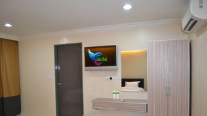 A hotel room with a flat-screen TV mounted on the wall, a wooden wardrobe, a bedside table with a remote control, and a bathroom mirror. - Safari Hotel (Ampang)