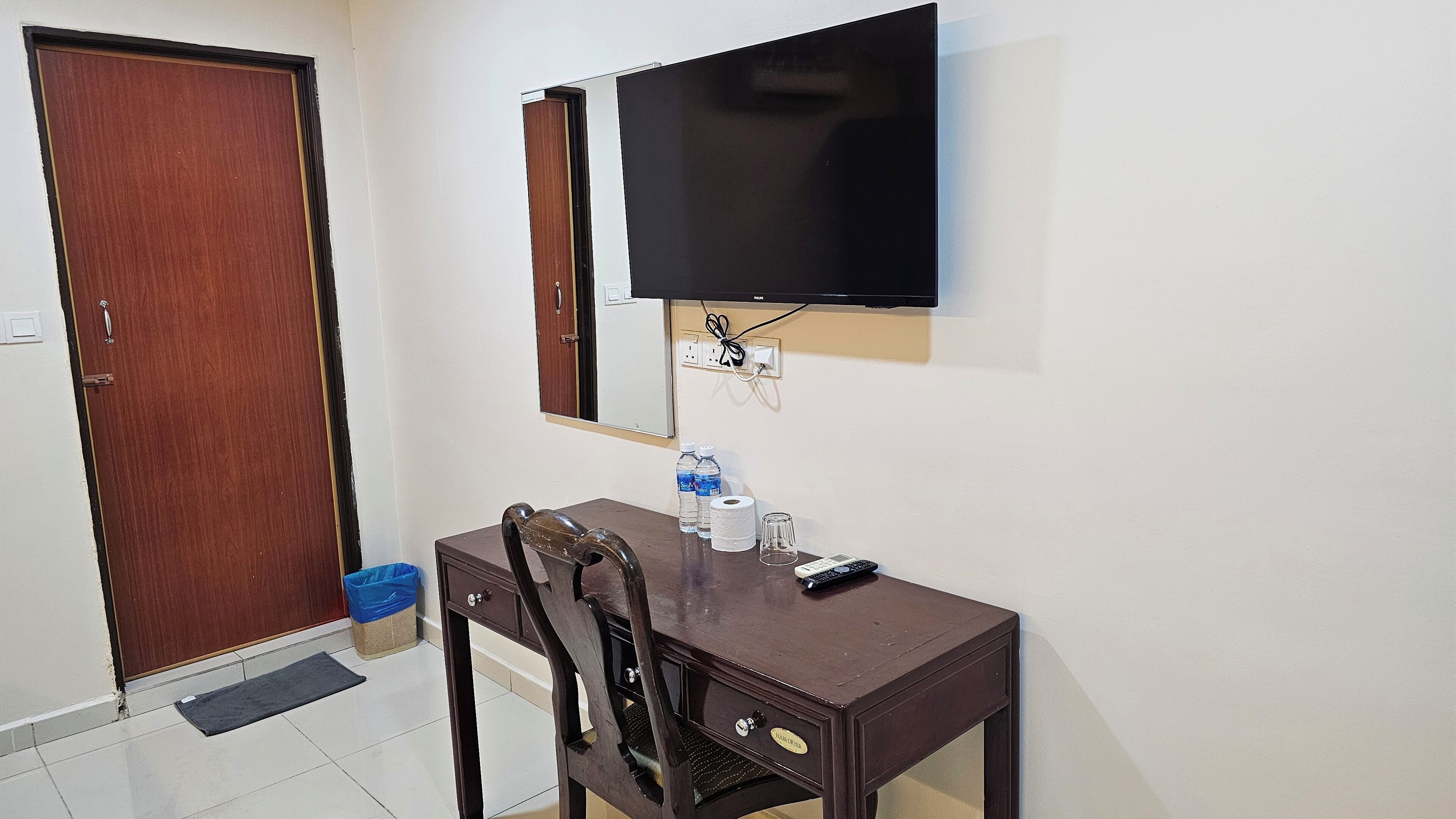 Een kamer met een houten bureau, een stoel, een aan de muur bevestigde televisie en een deur.