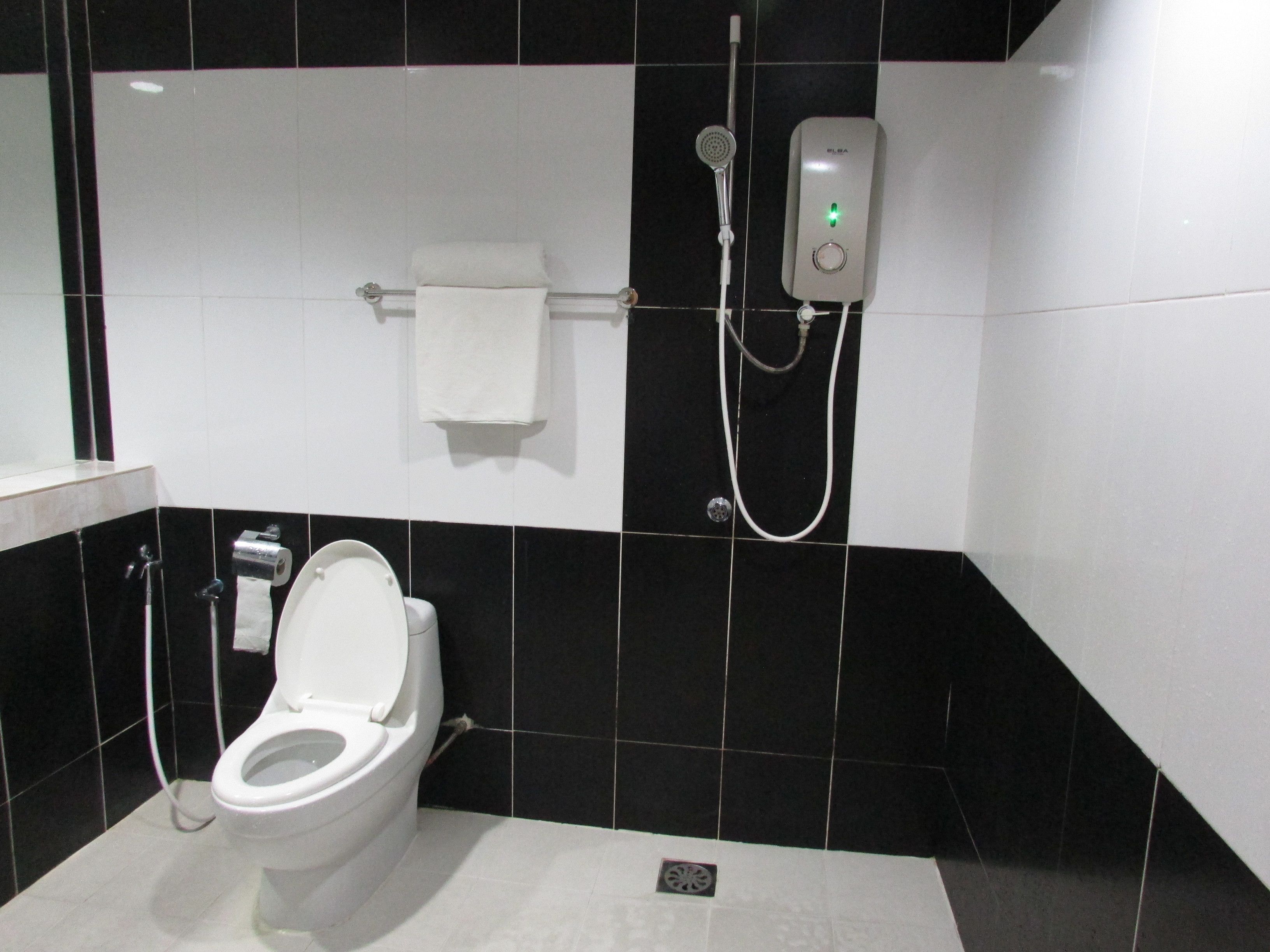 A bathroom with a toilet, a towel rack, a showerhead, and a soap dispenser.