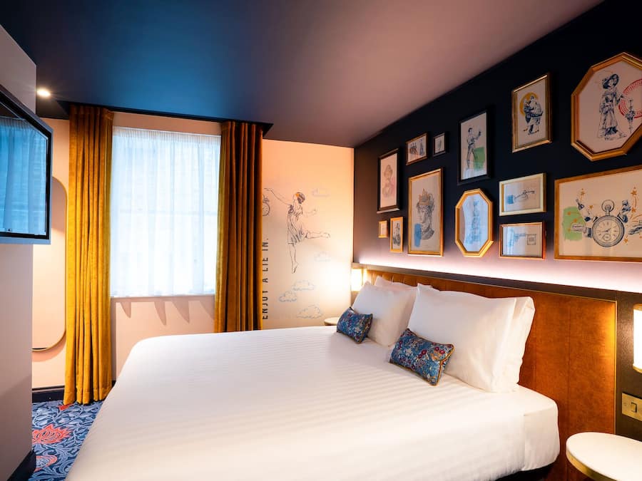 Une chambre d’hôtel avec un grand lit, une télévision et un mur décoré d’œuvres d’art encadrées.