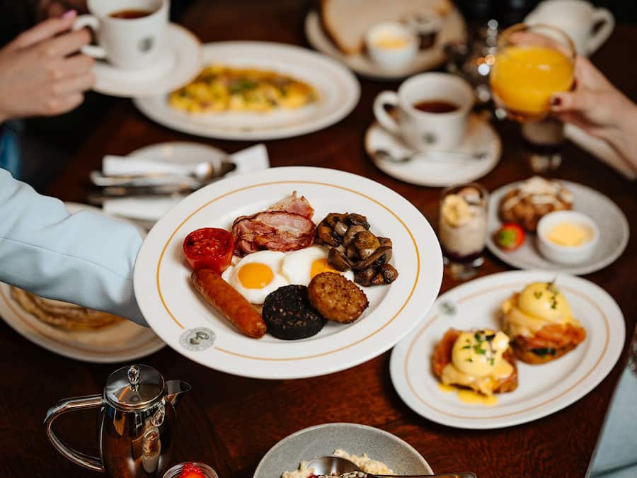 Une table mise pour le petit-déjeuner, avec des assiettes remplies de nourriture, des tasses et une théière.
