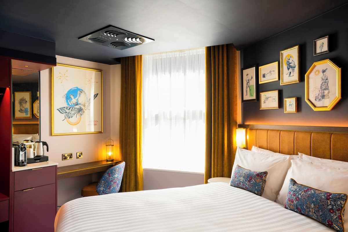 Une chambre d’hôtel avec un grand lit, une table de chevet avec une lampe, une armoire et des œuvres d’art accrochées aux murs.