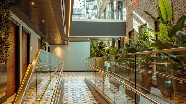 Un interior moderno con piso estampado geométrico, barandas de vidrio y pared de ladrillo.