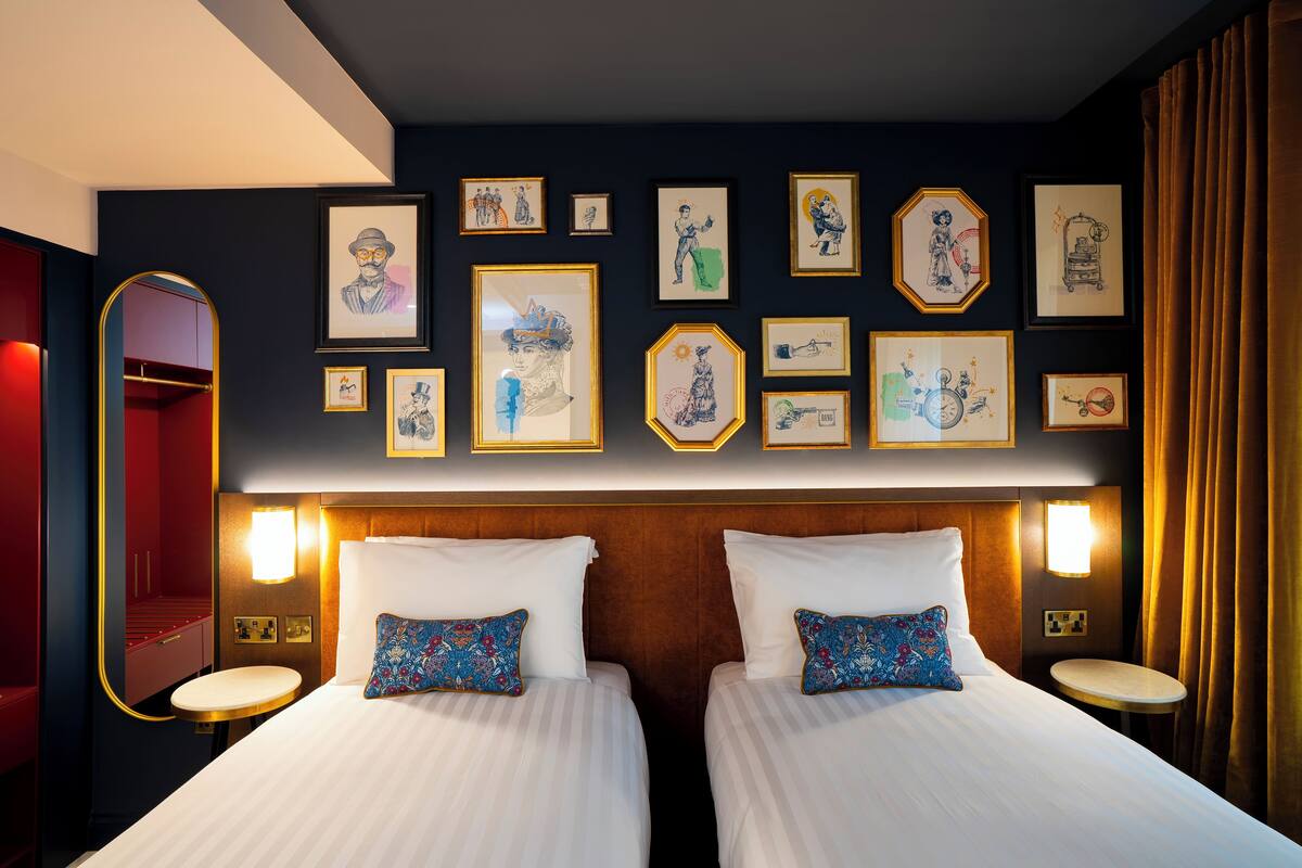 Une chambre d’hôtel avec deux lits, un grand miroir et des œuvres d’art accrochées aux murs.