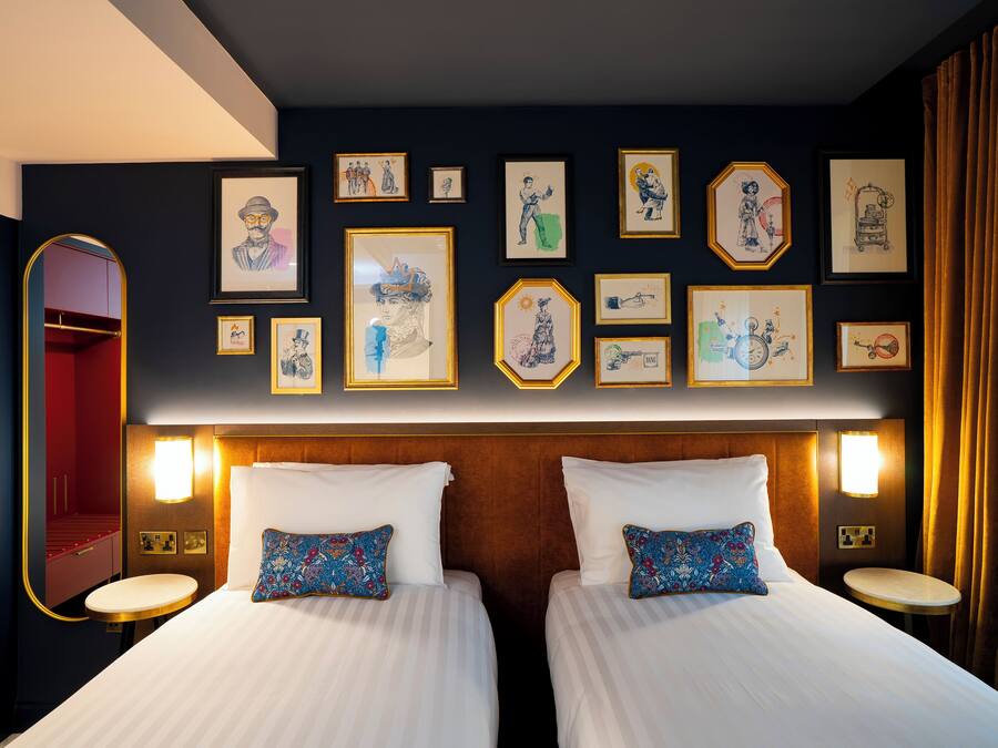 Une chambre d’hôtel avec deux lits, un grand miroir et des œuvres d’art accrochées aux murs.